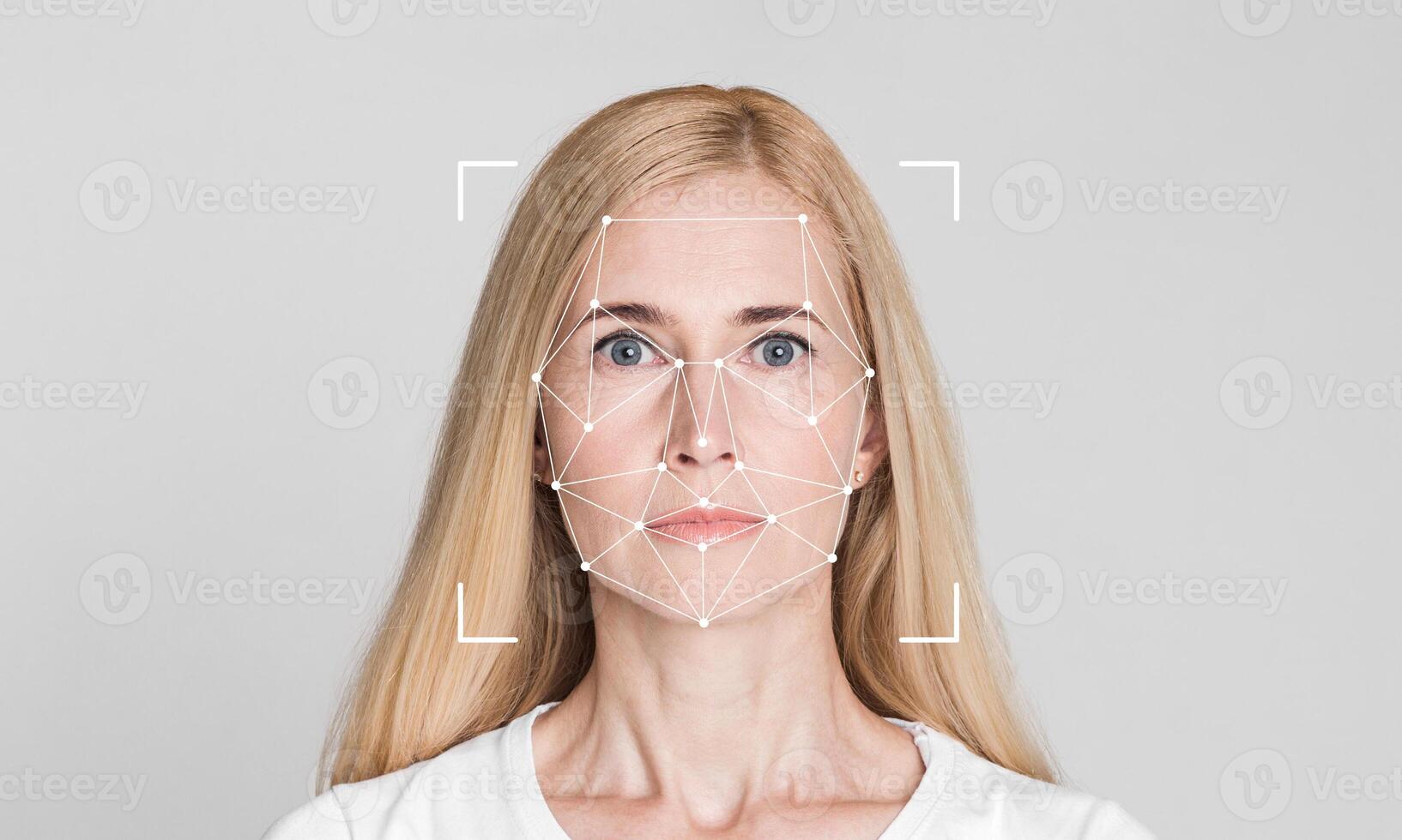 A woman with long blonde hair stares directly at the camera, demonstrating facial recognition technology. The background is plain, emphasizing the facial mapping overlay for identification. photo