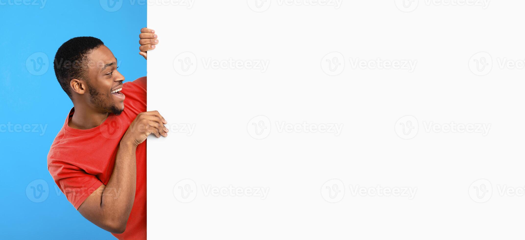 Discount Offer. Excited Black Man Looking At Empty White Board Posing Near Big Poster With Free Space Over Blue Background. Advertisement Banner With Man Advertising Your Text. Mockup, Panorama photo