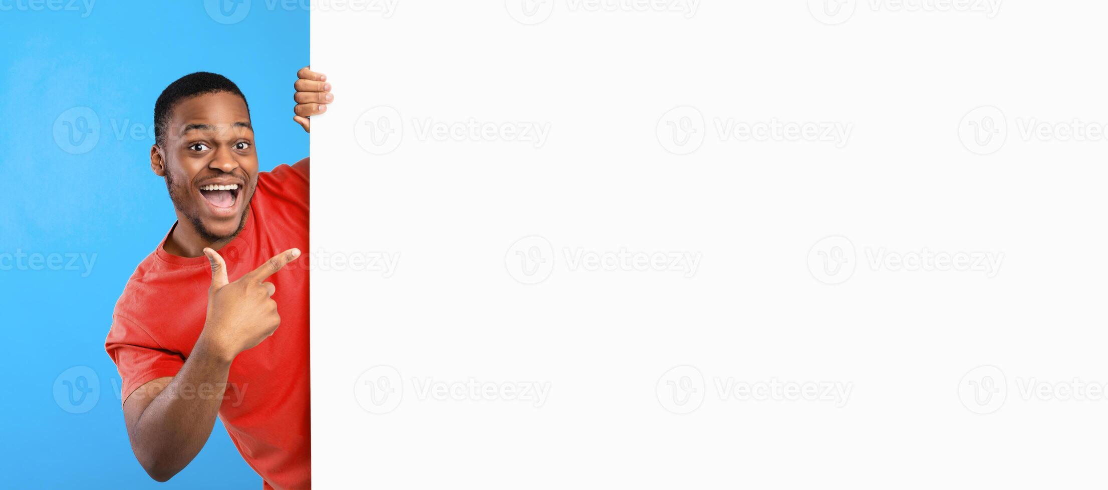 Great Sales Offer. Excited African American Man Pointing Finger At Copy Space On Big White Paper Poster Advertising Your Text Over Blue Studio Background, Smiling To Camera. Panorama, Mockup photo