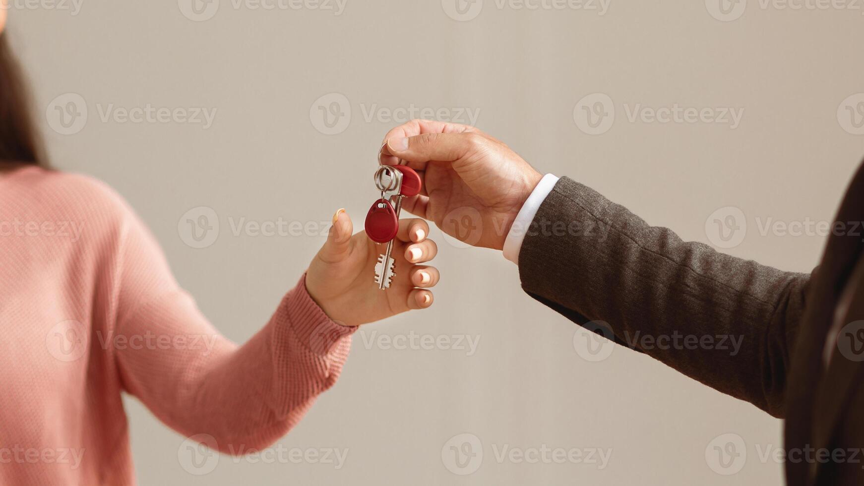 Handover Concept. Close up cropped view of professional real estate agent wearing suit holding in hand and giving keys to young lady buyer. Woman taking key of future new apartment photo