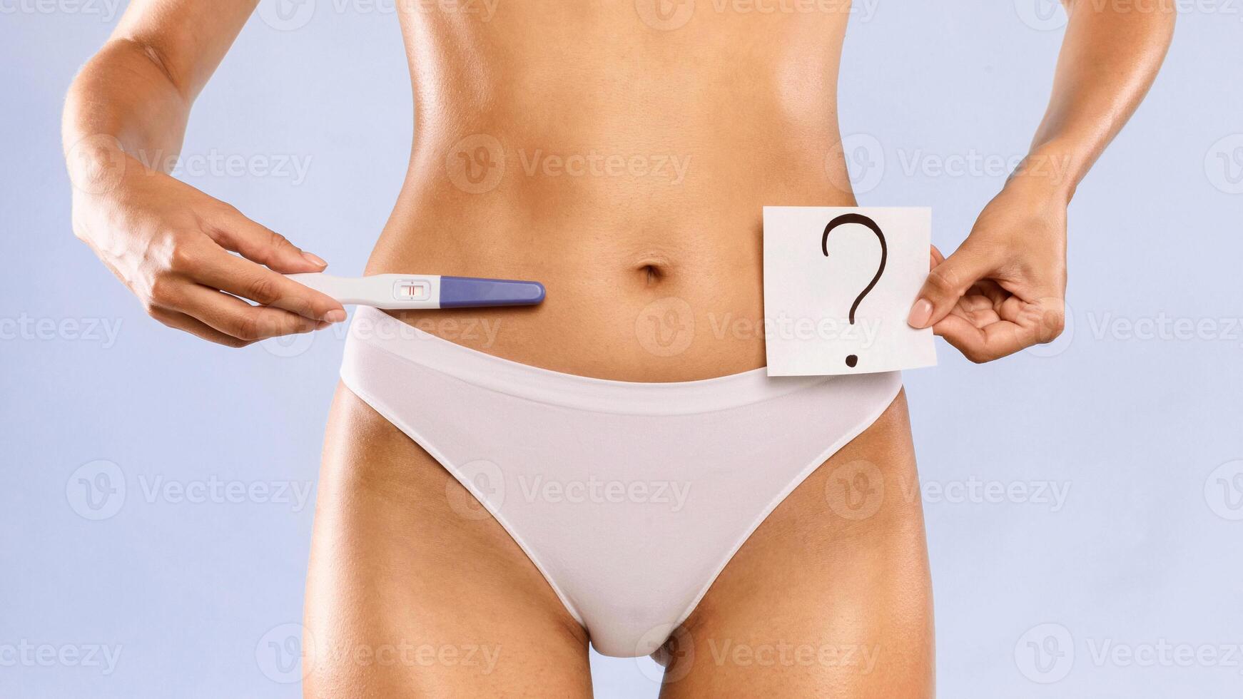 Young woman holding pregnancy test with two stripes and sticker post-it note card with question mark. Positive result. Unrecognizable female guessing unborn baby gender or thinking about abort photo