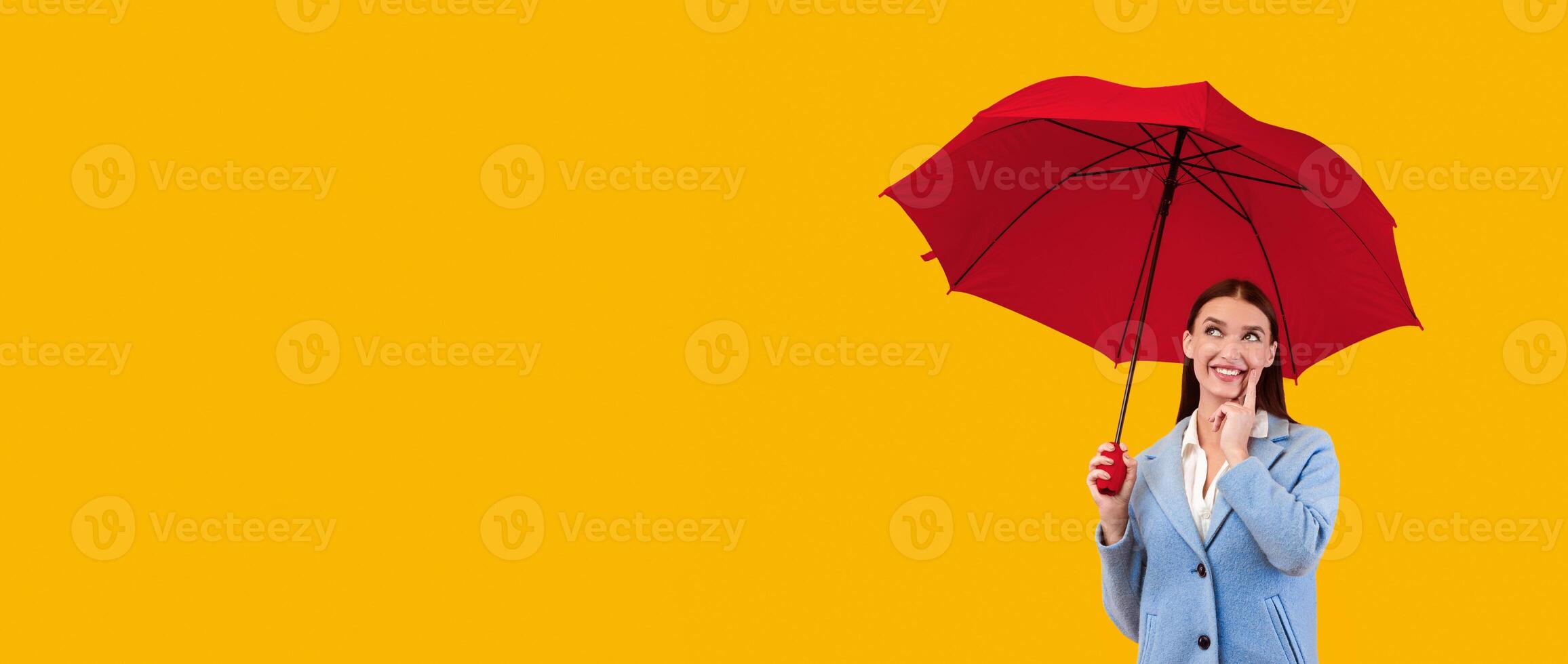 Full length portrait of dreamy lady standing under yellow umbrella at studio, thinking and looking up photo