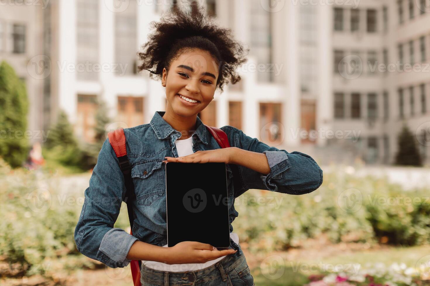Black College Student Girl Showing Tablet With Empty Screen Smiling To Camera Standing Outdoors Near University Building. Young Lady Advertising Educational Website. Mockup, Selective Focus photo