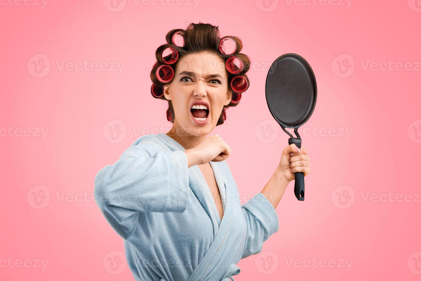 Angry Woman Shouting Holding Frying Pan Threatening Looking At Camera Standing Over Yellow Studio Background. Crazy Housewife, Domestic Violence And Aggression. Mad Wife Shouting Tired Of Cooking photo