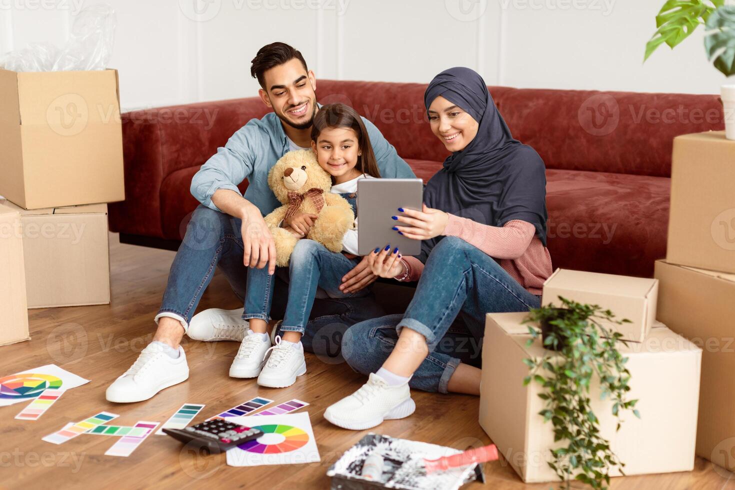 Modern Remote Communication Concept. Portrait of positive arabic family making virtual call with friends or grandparents using tablet, sitting on floor carpet with paint, talking online photo