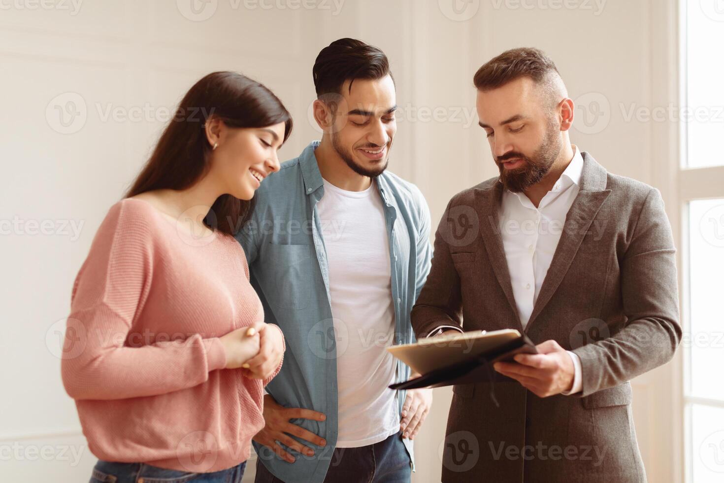 Buying New House. Smiling young Arab spouses discussing agreement with real estate agent or broker. Professional financial advisor or salesman explaining contract details to clients at meeting photo