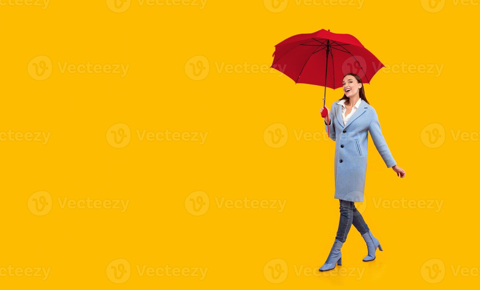 Nice Day. Excited young model in blue coat walking with bright umbrella, isolated on pastel pink studio wall, copy space photo