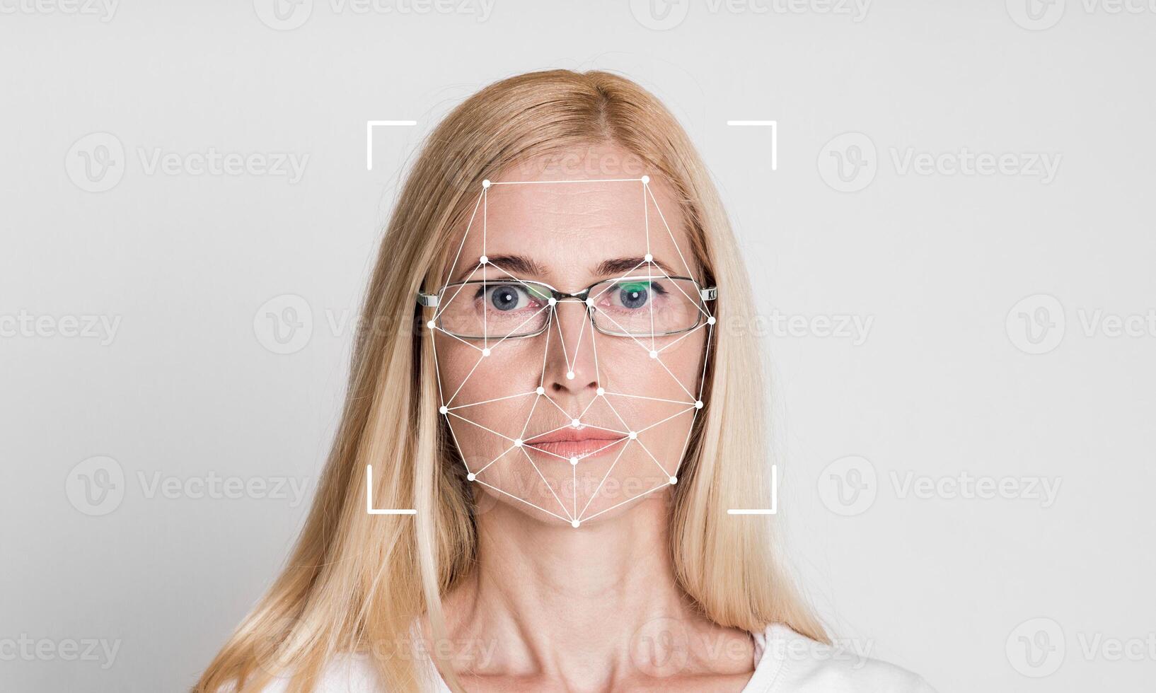 A woman with long blonde hair and glasses is positioned against a blank backdrop. Facial recognition technology highlights her features, showcasing modern identification methods in action. photo