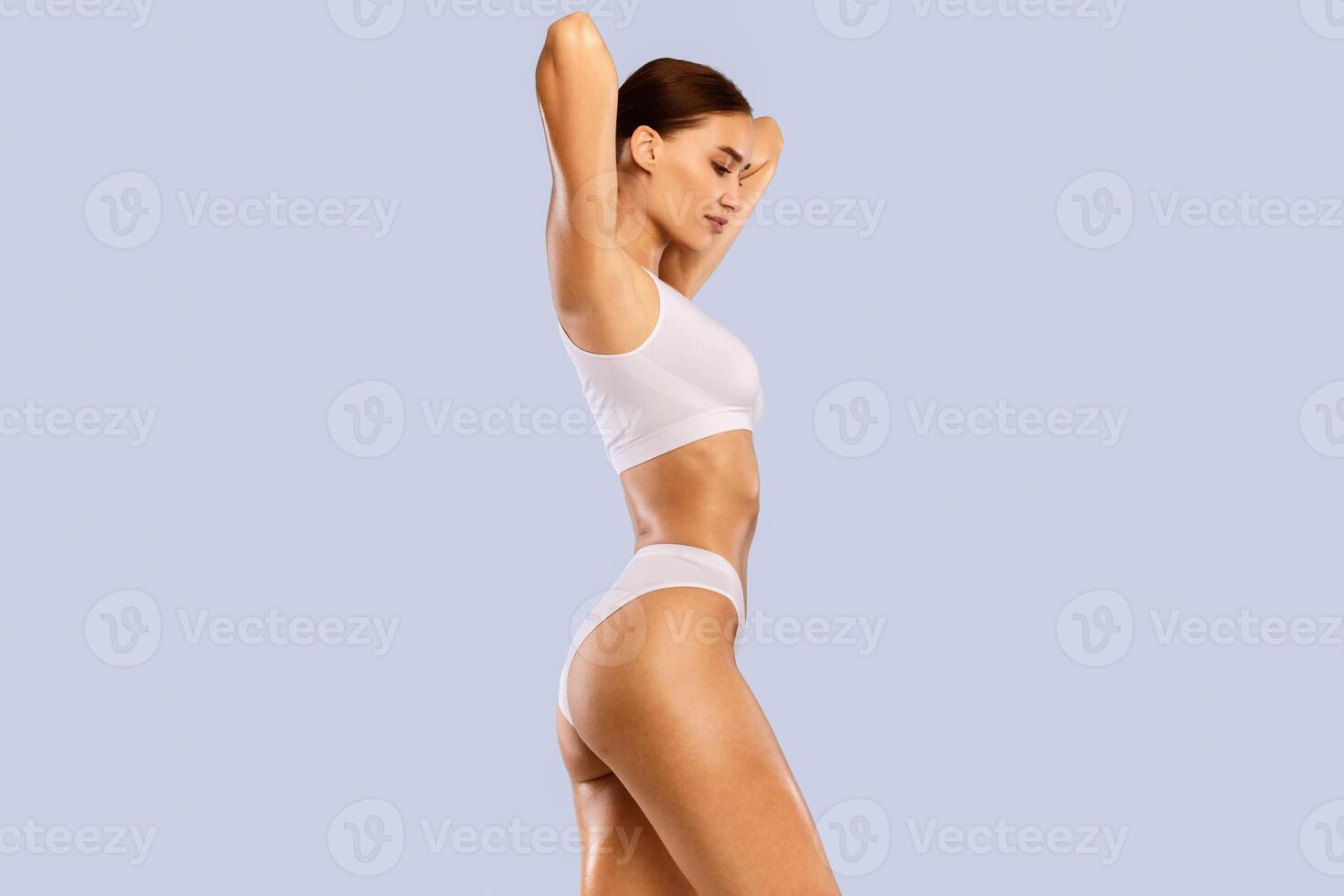 Bodycare Concept. Profile Side View Portrait Of Slim Woman With Perfect Ideal Body Shape Posing With Raised Arms Isolated On Blue Studio Background, Wearing White Top And Panties, Free Copy Space photo