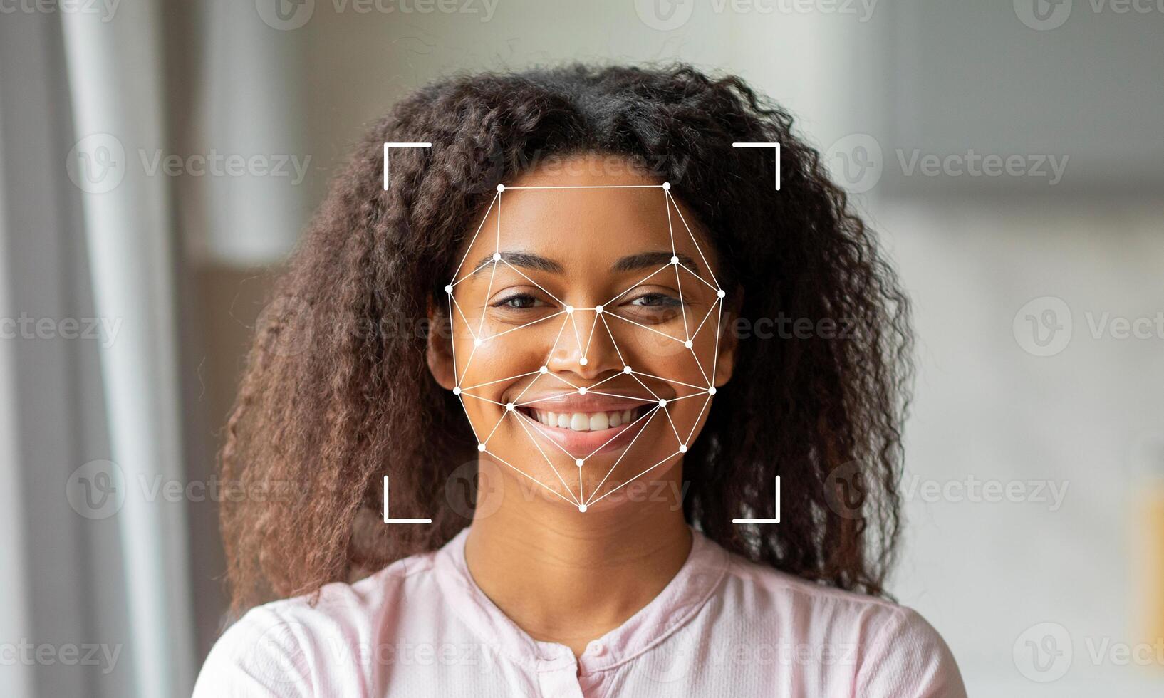 A woman with curly hair smiles brightly, showcasing her facial features. Overlayed graphics suggest facial recognition technology is being used. The setting is well-lit and inviting. photo