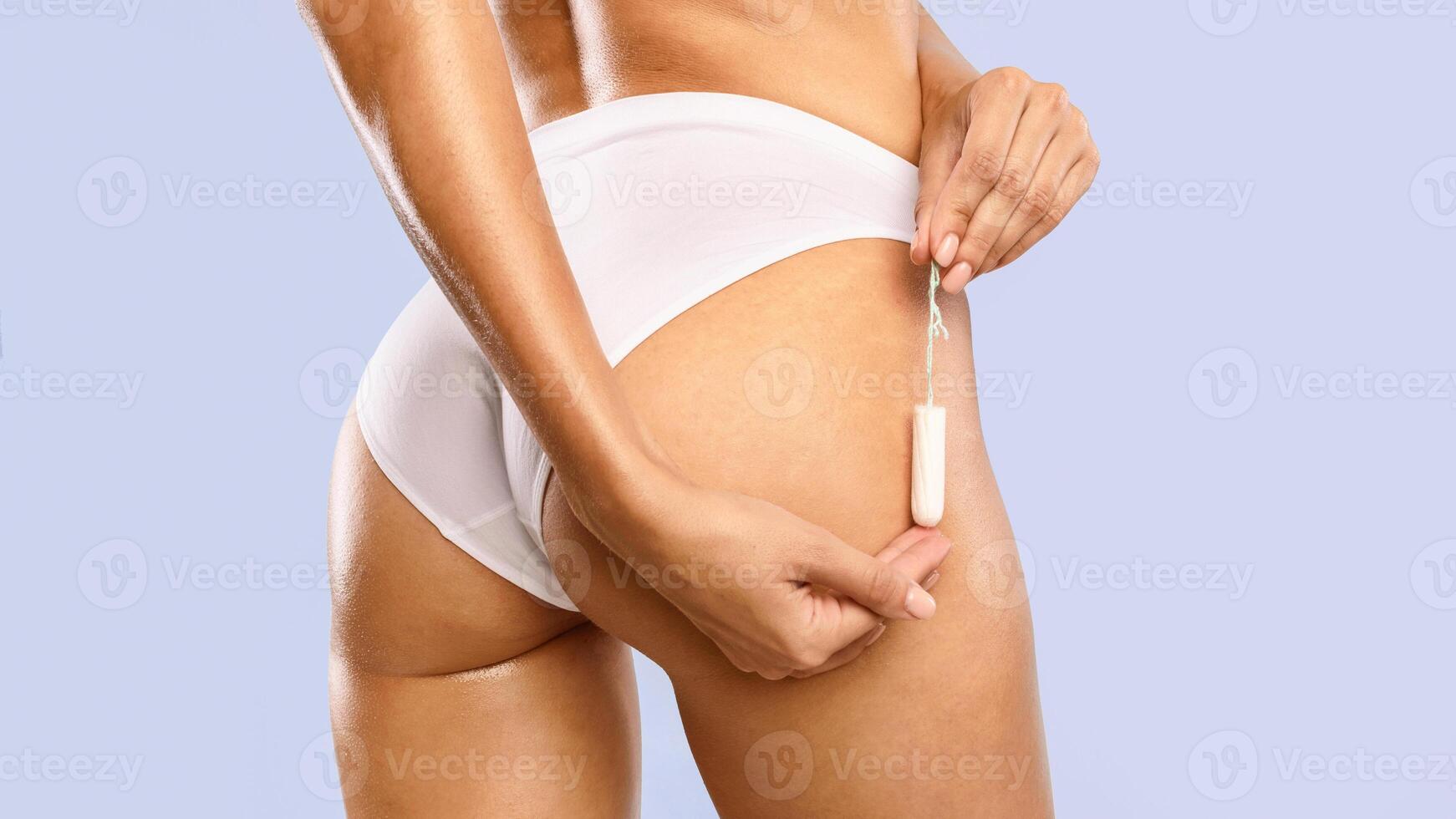 Closeup cropped view of unrecognizable young woman in white panties holding absorbent tampon neak buttocks, rear back view, isolated on blue studio background, banner. Menstrual Cycle photo