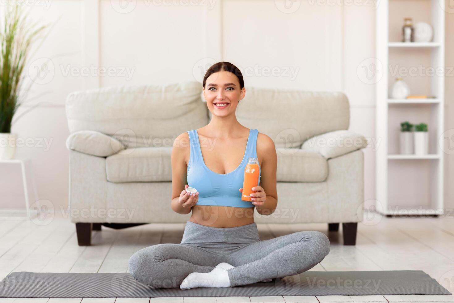 Healthy Life. Fitness Woman Holding Bottle Of Fruit Juice Smiling To Camera Sitting On Rolling Mat During Training At Home photo
