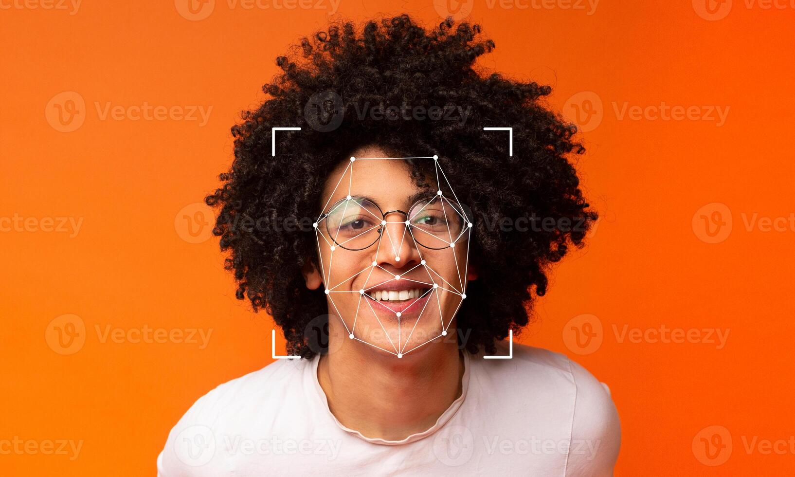 A person with curly hair and glasses smiles confidently against a vibrant orange background. Facial recognition markers highlight their features, demonstrating modern ID technology. photo