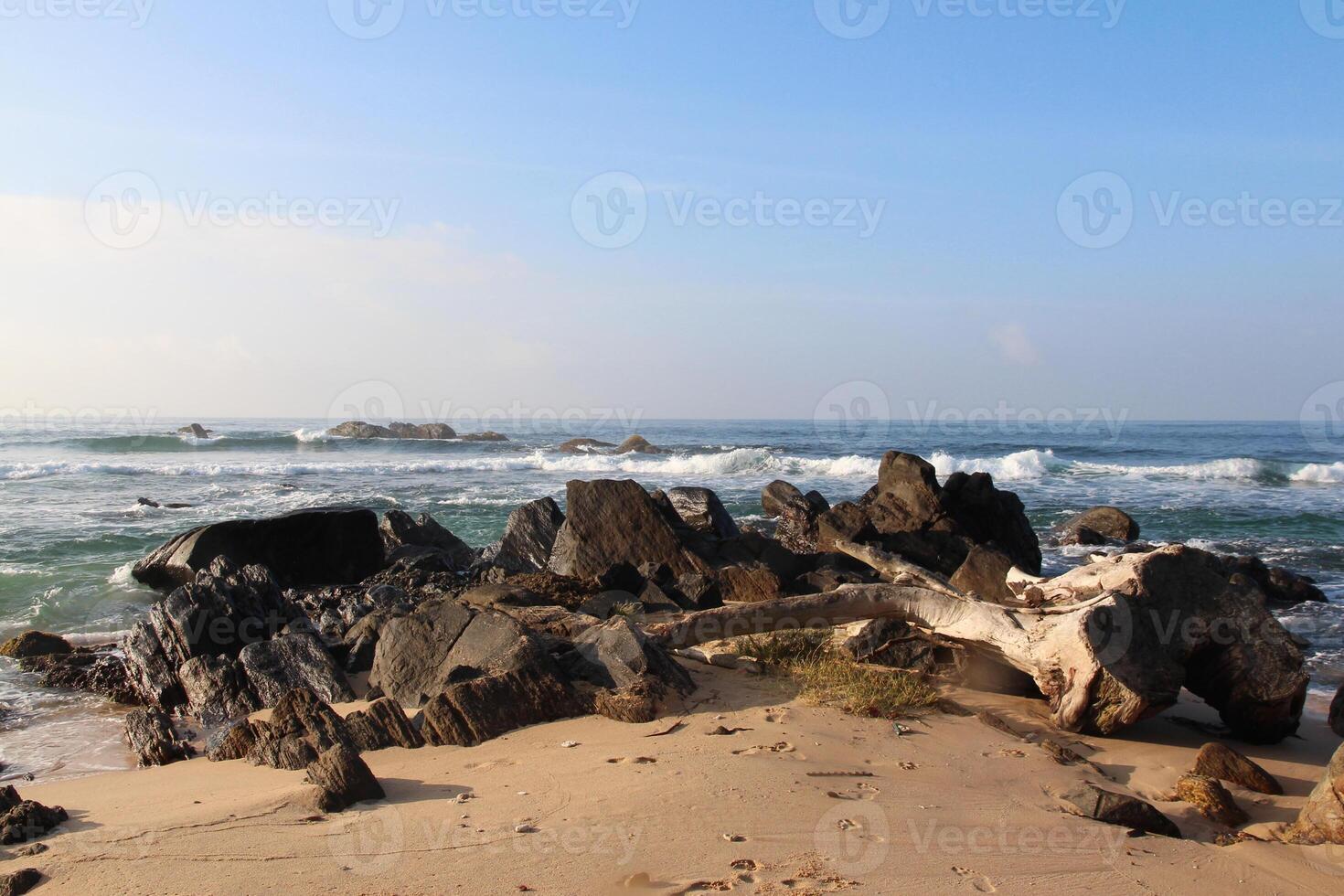 Sunny coastal landscape with golden sand, rough rocks and gentle waves washing the shore. Calm seaside landscape. Nature background, wallpaper photo