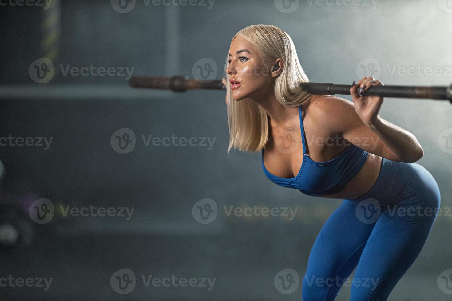 young female athlete showcases her strength and determination as she performs squats barbell in well lit gym environment. Her concentration highlights dedication fitness photo