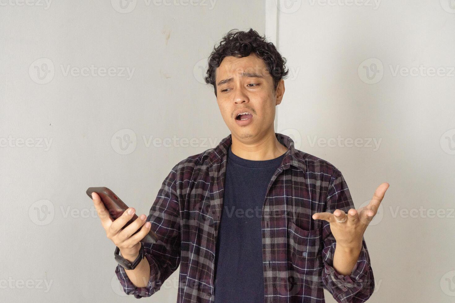 Frustrated Man Looking at His Smartphone. A man looks at his phone with a frustrated expression. He seems upset or confused by something on the screen. photo