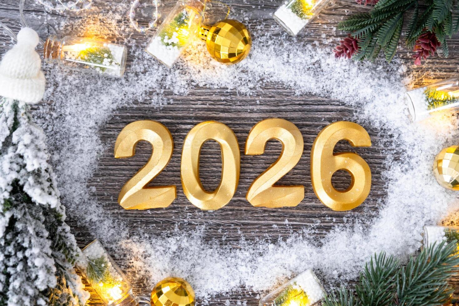 Happy New Year golden numbers 2026 on grey wooden background with Christmas tree, snow, lights of garlands. Greetings, postcard. Calendar, cover photo