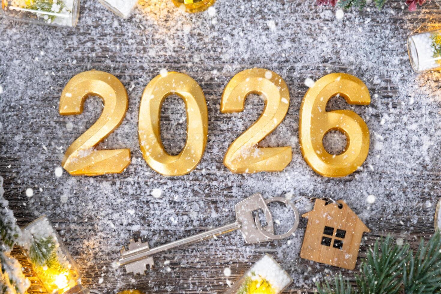 New Year 2026 golden numbers and House key with tiny form of home on festive grey wooden background flatlay, lights of garlands, greeting card. Housing, real estate, relocation, mortgage, insurance. photo