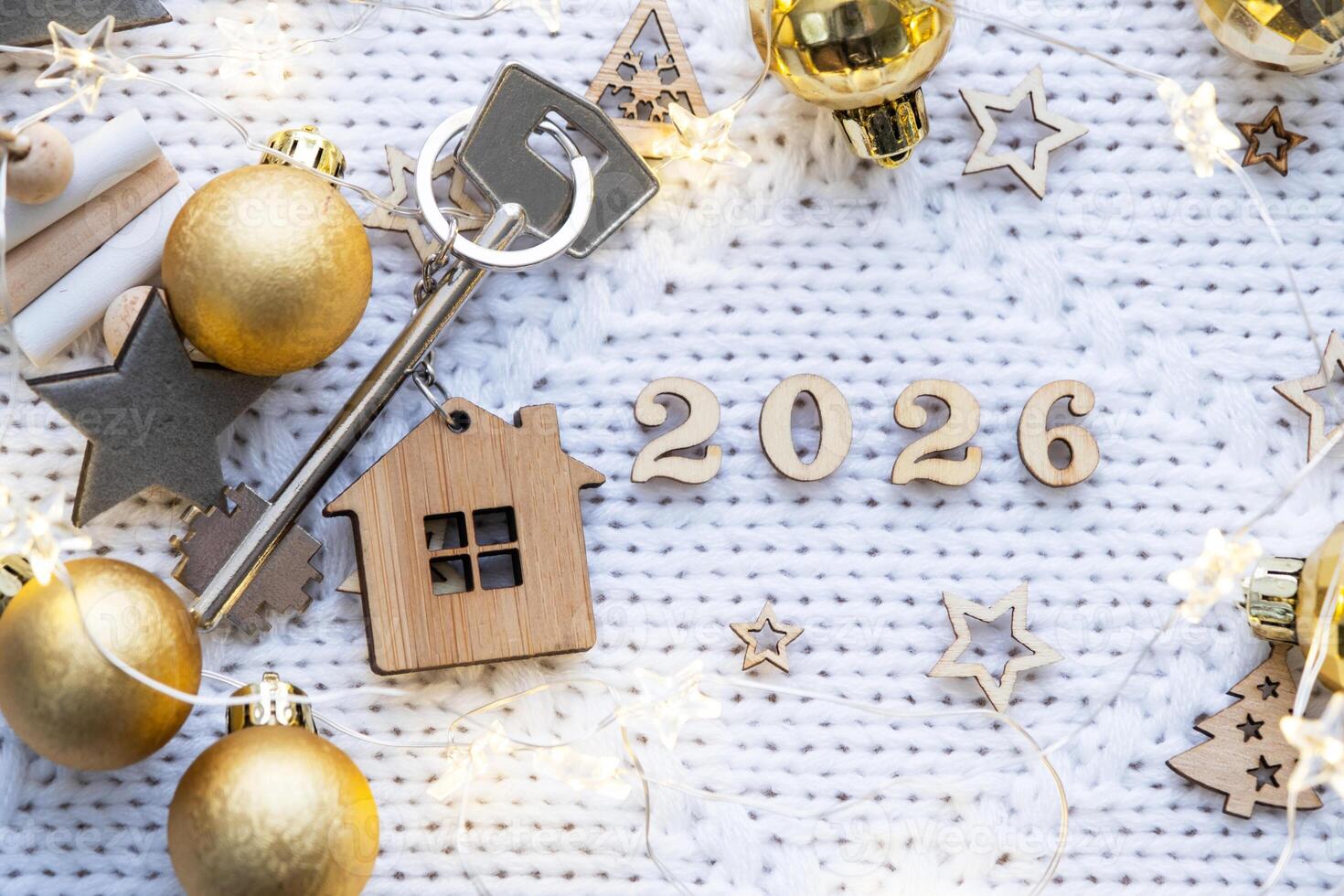 House key with keychain cottage on festive background with stars, lights of garlands. New Year 2026 wooden letters, greeting card. Purchase, construction, relocation, mortgage, insurance photo