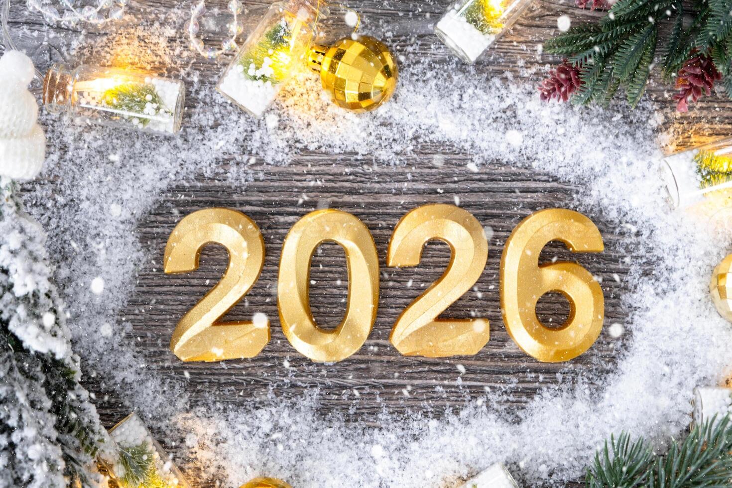 Happy New Year golden numbers 2026 on cozy grey wooden background with Christmas tree, snow, lights of garlands. Greetings, postcard. Calendar photo