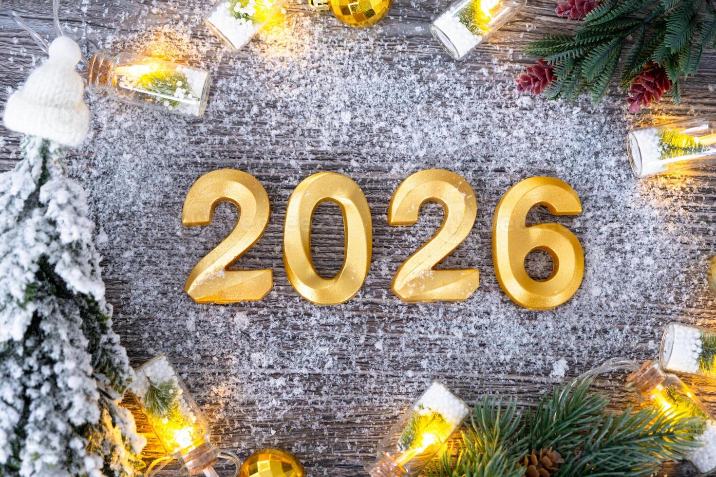 Happy New Year golden numbers 2026 on cozy grey wooden background with Christmas tree, snow, lights of garlands. Greetings, postcard. Calendar, cover photo