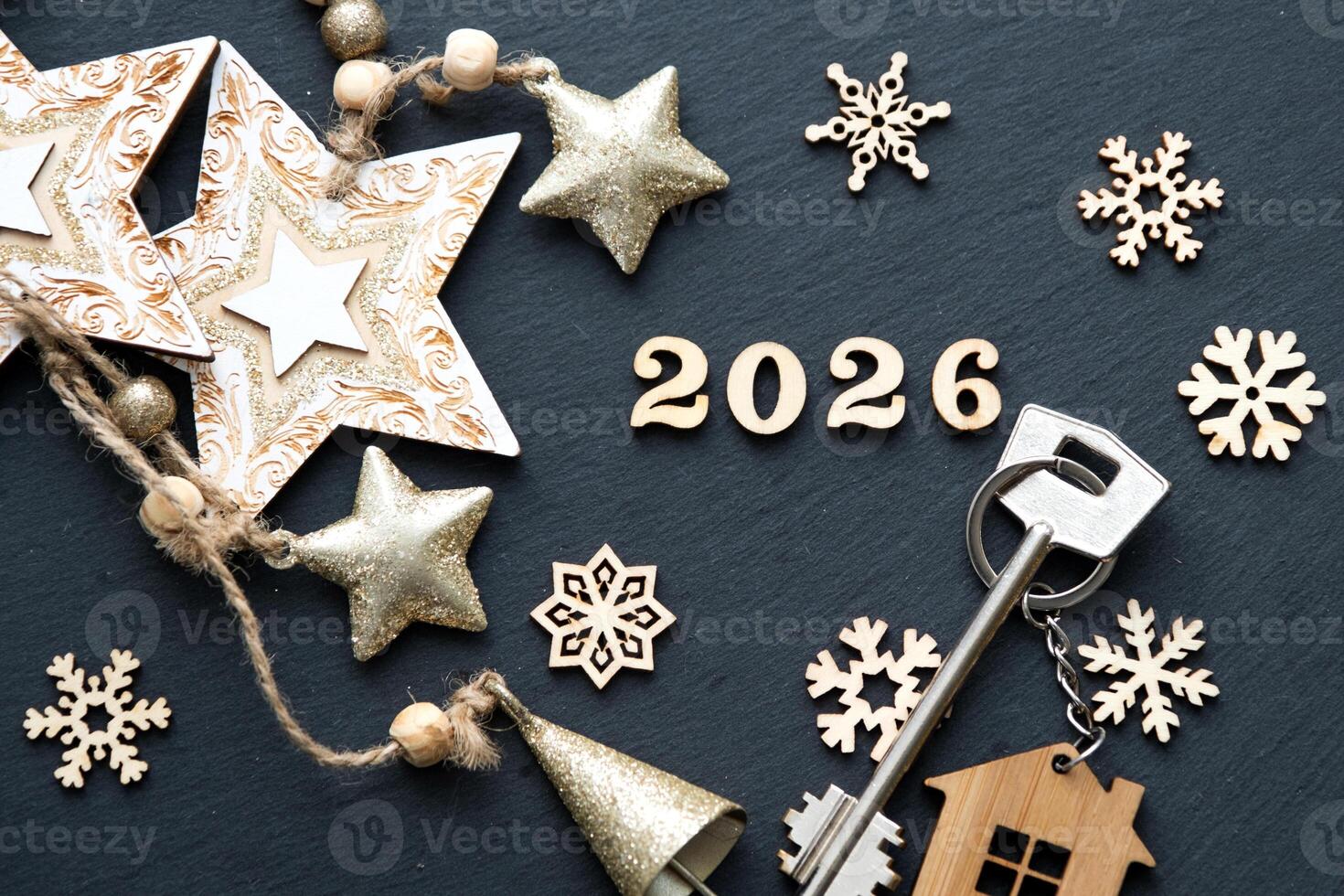House key with keychain cottage on festive black background with stars, lights of garlands. New Year 2026 wooden letters, greeting card. Purchase, construction, relocation, mortgage, insurance photo