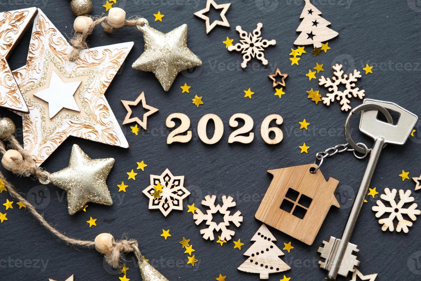 House key with cottage on festive black background with stars, lights of garlands. New Year 2026 wooden letters, greeting card. Purchase, construction, relocation, mortgage, insurance photo