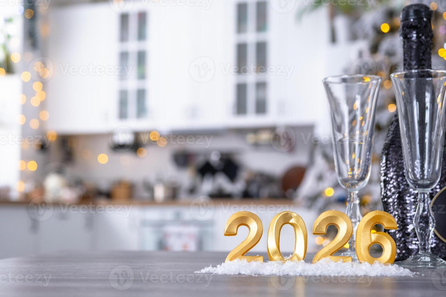 number 2026 bottle sparkling wine and glasses on table of cozy white kitchen with Christmas tree and garland lights. Housing, interior, renovation, mortgage, rent in New Year photo