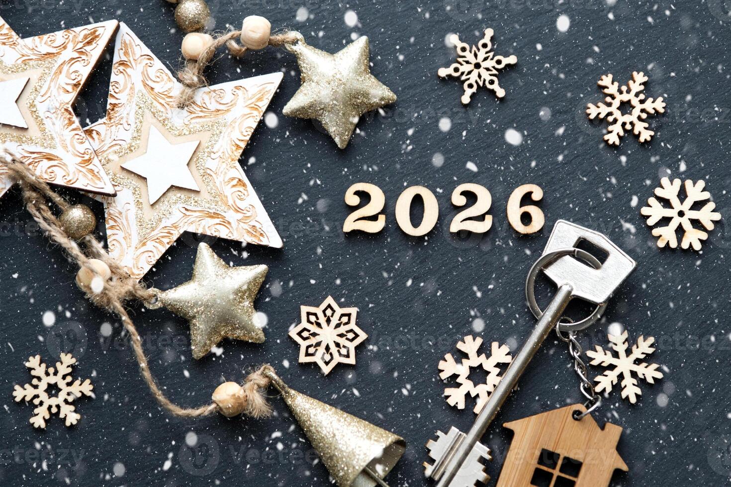 House key with keychain cottage on festive black background with stars, lights of garlands. New Year 2026 wooden letters, greeting card. Purchase, construction, relocation, mortgage photo