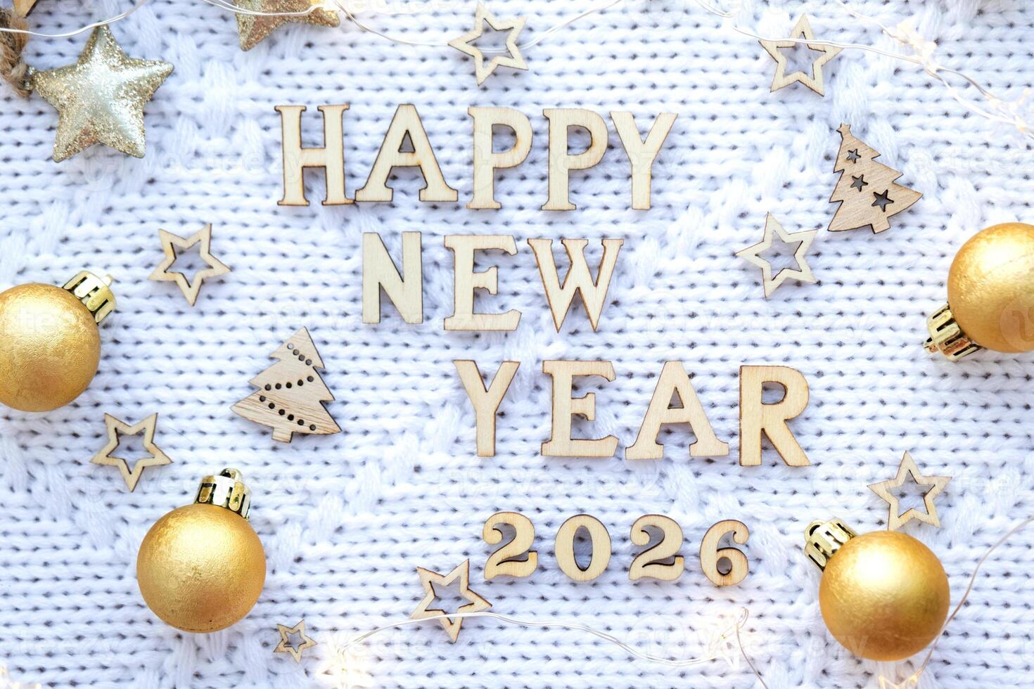 Happy New Year wooden numbers 2026 on cozy festive white knitted background with sequins, stars, lights of garlands. Greetings, postcard. Calendar, photo