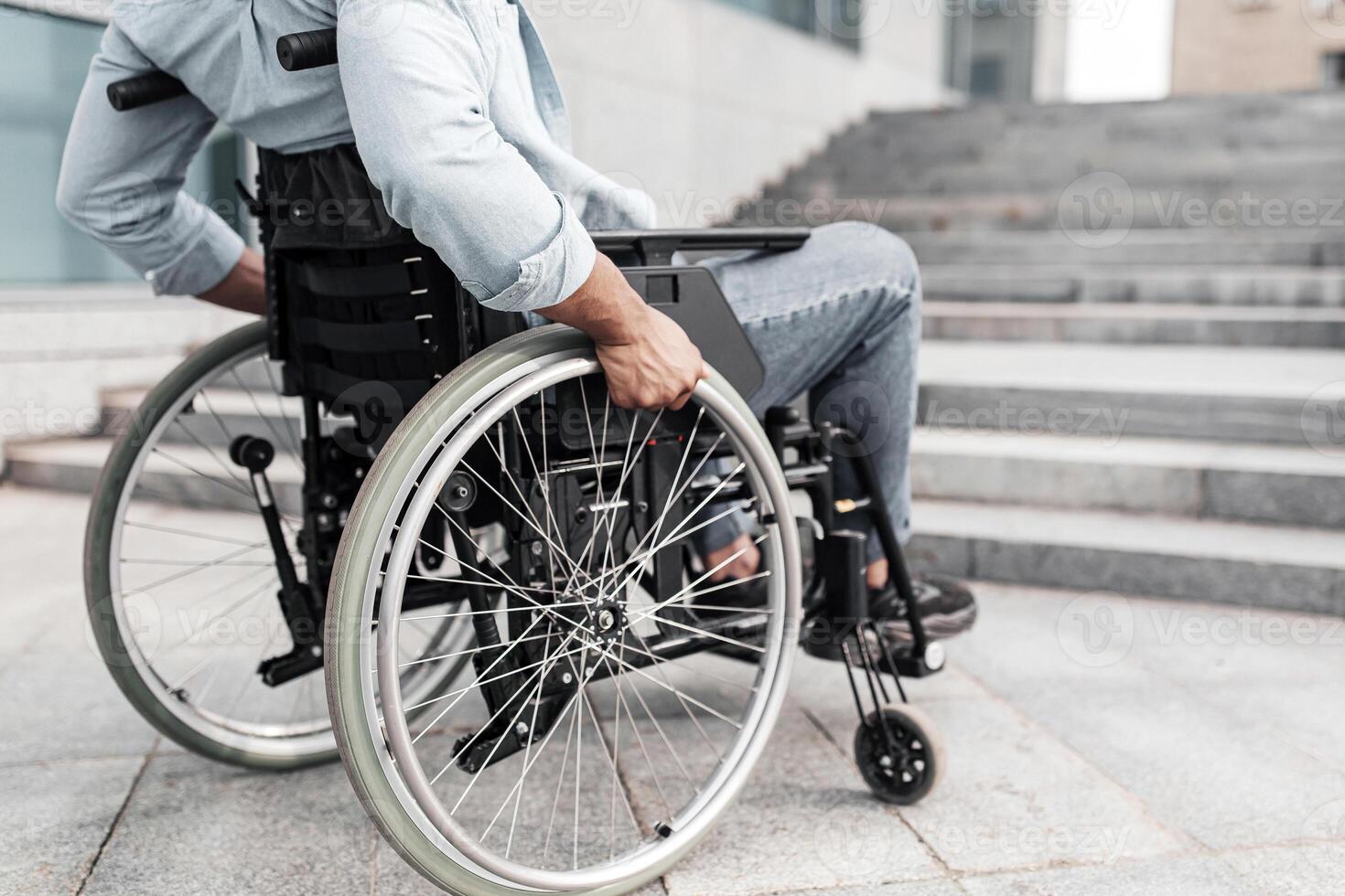 Disability and accessible environment problems. Unrecognizable young black man in wheelchair standing in front of stairs without ramp, having no possibility to enter building, free space photo