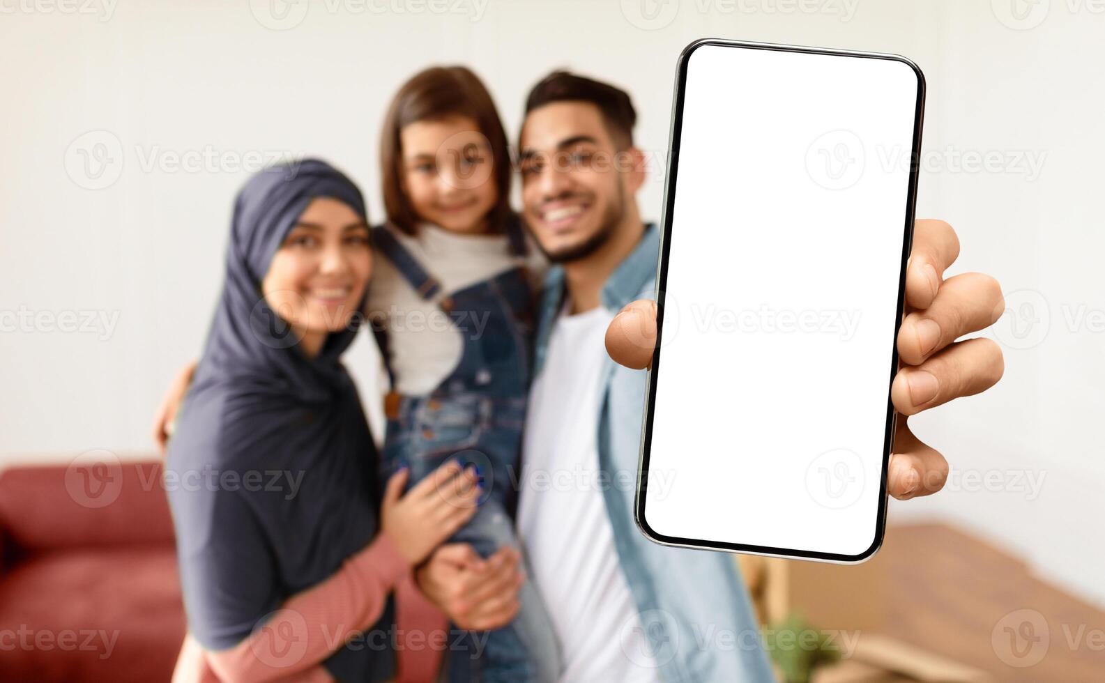 House Ownership. Happy Muslim Family Showing Key, Selective Focus On Hand. Cheerful Parents Hugging Little Kid, People Moving In New Apartment Standing In Living Room, Blurred Background photo