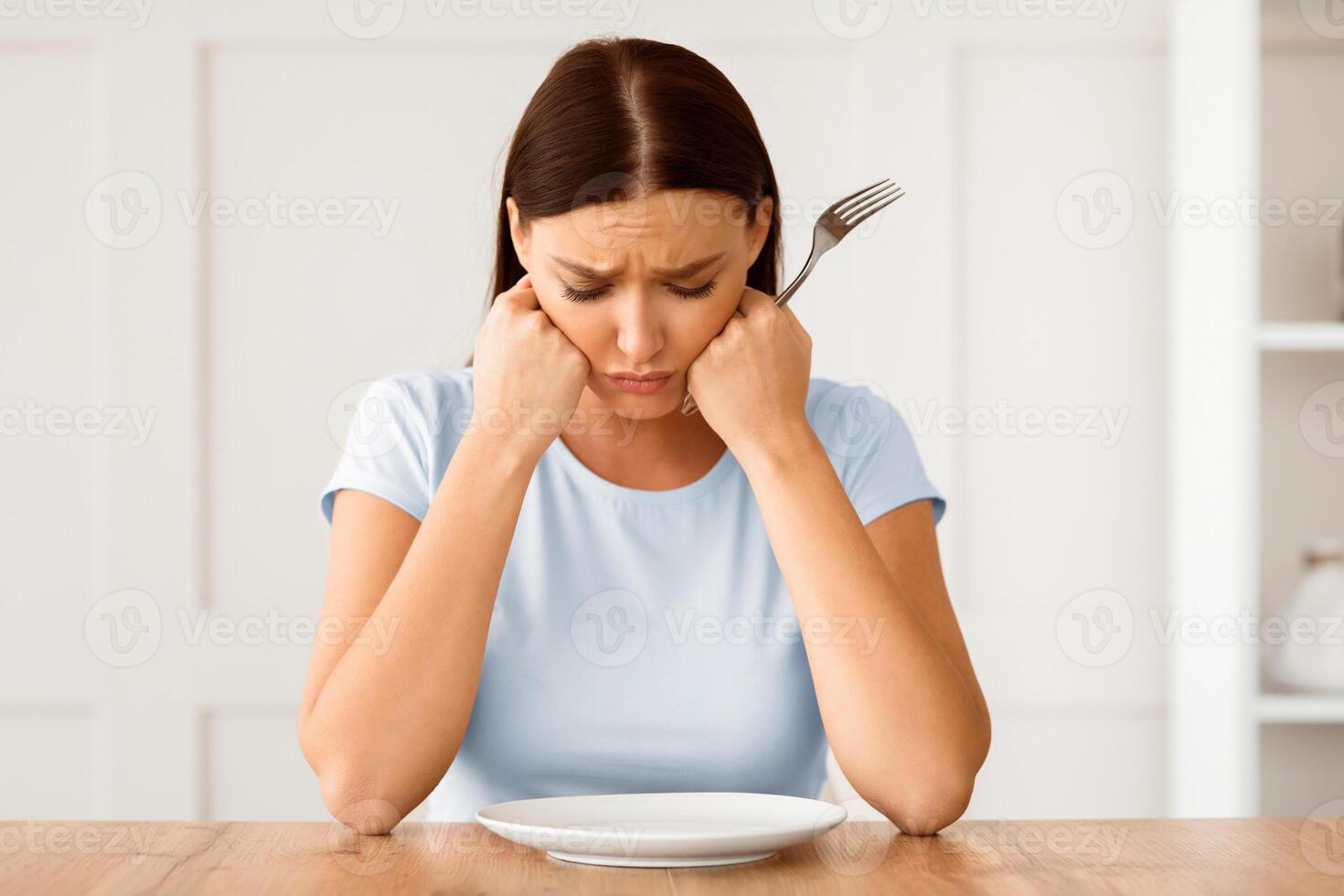 Dieting Concept. Unhappy Woman Looking At Empty Plate Losing Weight Sitting At Table At Home. photo
