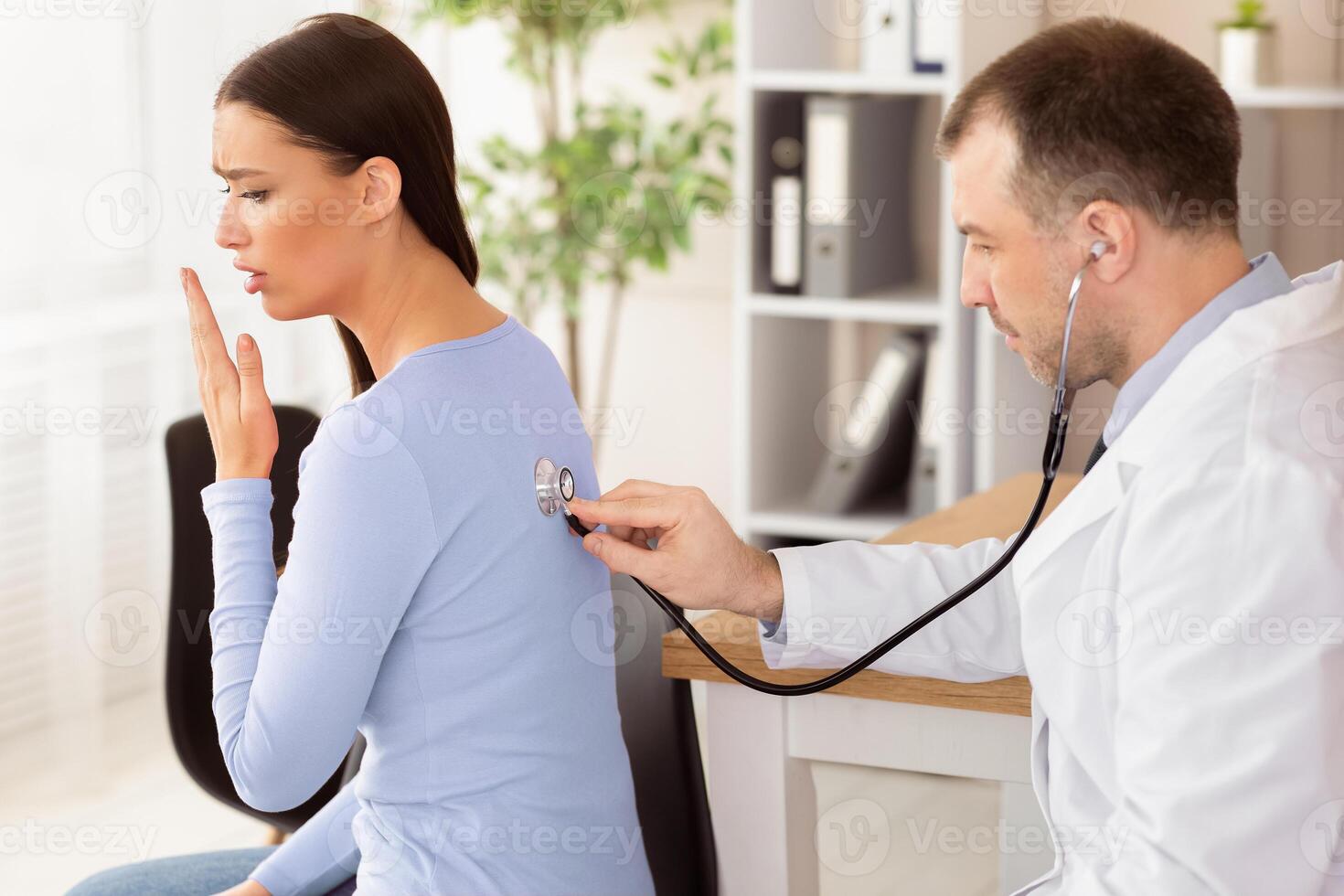 Check Up Concept. Mature experienced doctor checking breath of female patient, girl is coughing, side view photo
