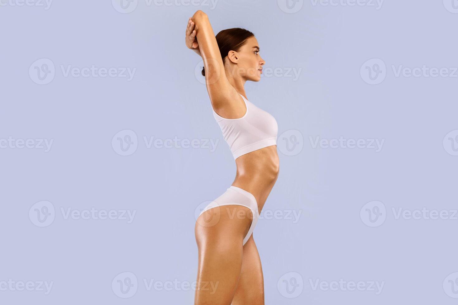 Profile Side View Portrait Of Beautiful Slim Lady With Perfect Ideal Body Shape Posing Isolated On Blue Studio Background, Lady In White Underwear Enjoying Herself, Standing With Raised Arms photo
