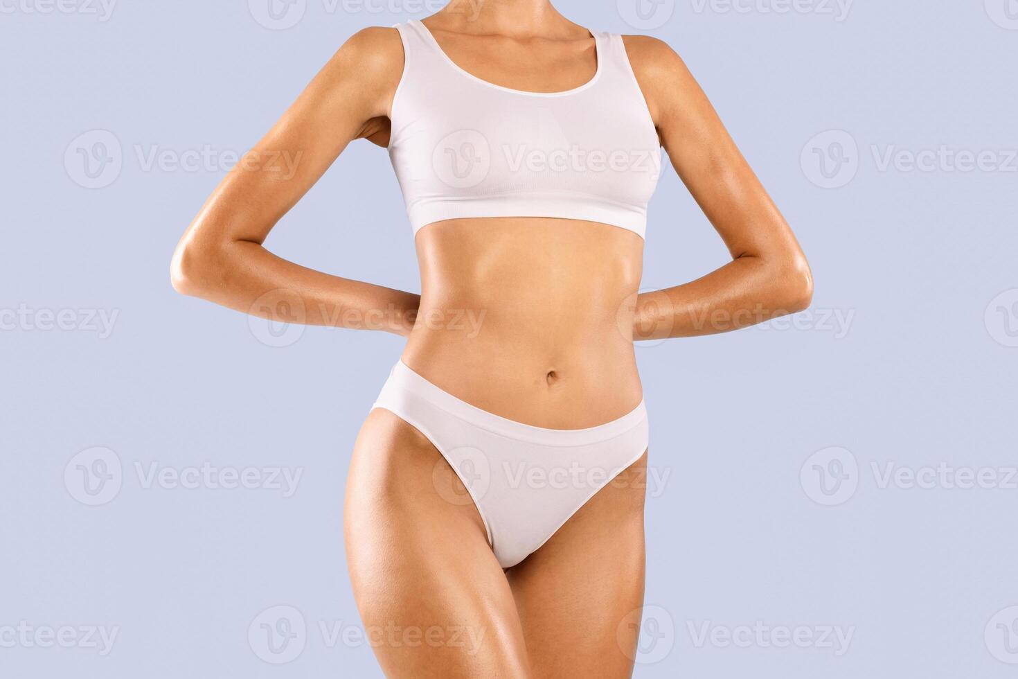 Closeup Cropped Frontal View Of Slim Lady With Perfect Body Shape And Flat Tummy Posing Isolated On Blue Studio Background, Woman Wearing White Lingerie Top Bra And Panties. Fitness, Diet Concept photo
