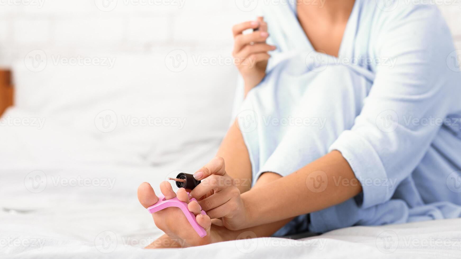 Unrecognizable Lady Doing Pedicure Caring For Nails On Legs Sitting In Bed At Home. Fingernails Care, Female Beauty Routine Concept. Cropped, Selective Focus, Panorama With Copy Space photo