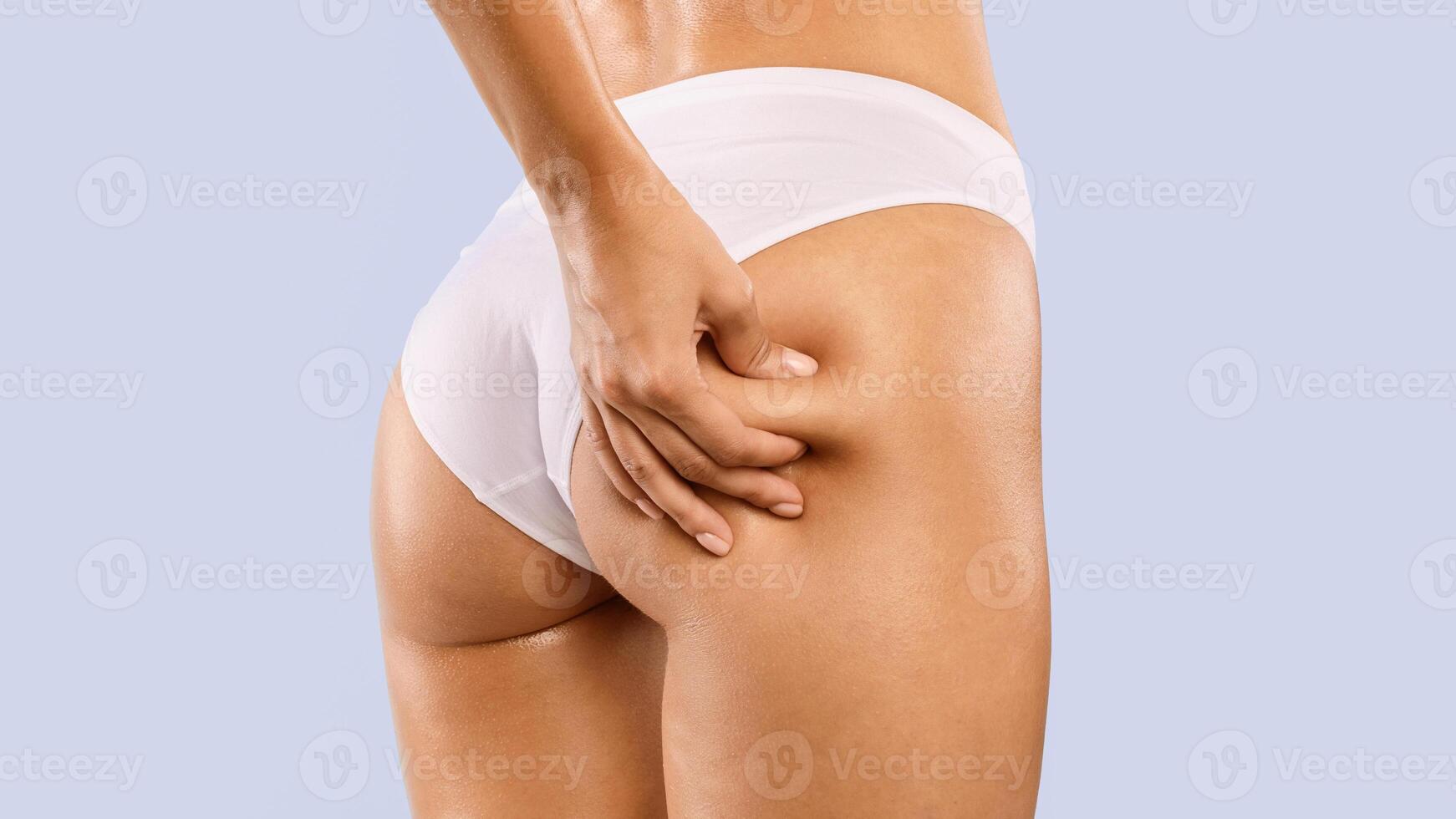 Skin Elasticity Check Concept. Closeup cropped view of unrecognizable young woman pinching her buttocks, examining cellulite, wearing white panties isolated on blue studio background photo