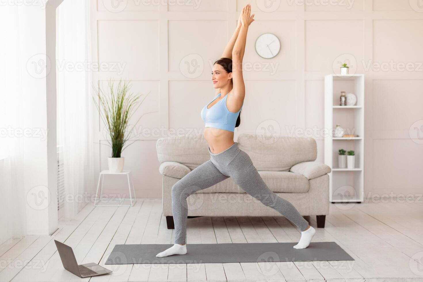 Online Yoga. Fit Girl Standing In Warrior Pose Exercising At Laptop At Home. Empty Space For Text photo