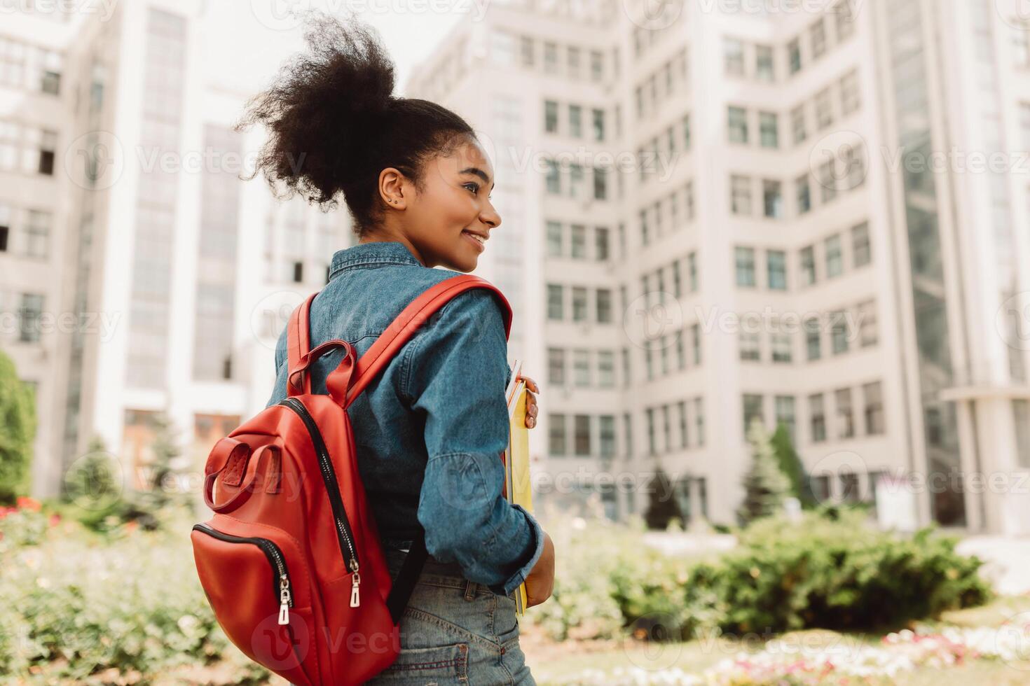 Happy African Student Girl Posing With Backpack Standing Back To Camera, Looking Aside Posing Near University Building Outside. Modern Study And Education, Studentship Concept photo