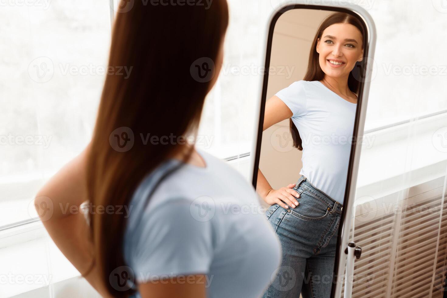 Perfect Weight. Happy Skinny Girl Looking At Reflection In Mirror Standing At Home. Successful Slimming Concept. Selective Focus photo