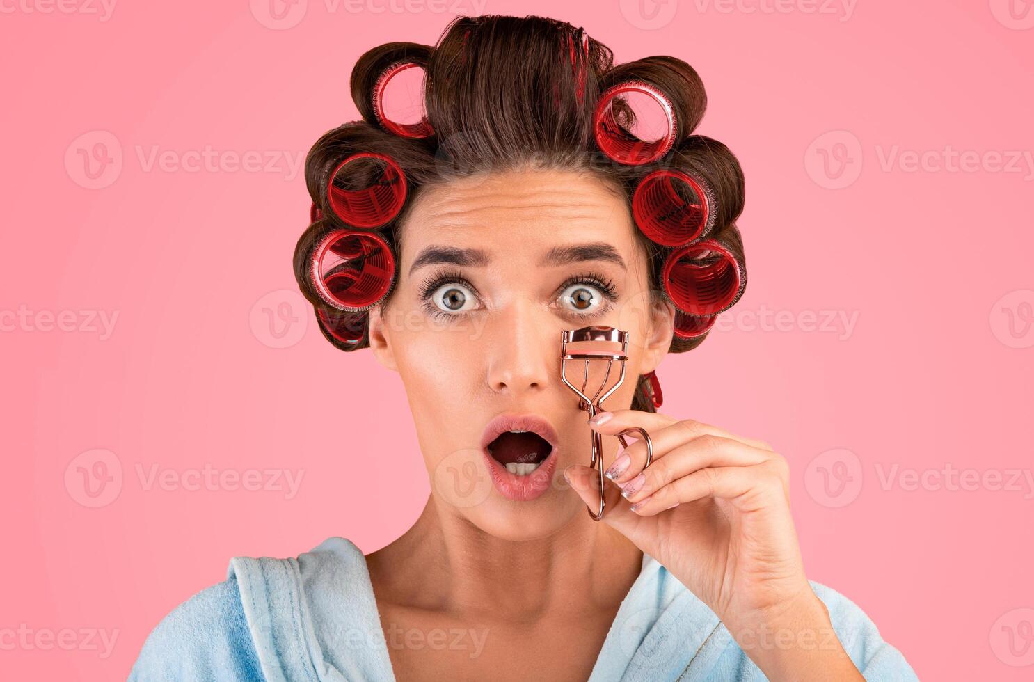 Shocked Housewife Holding Eyelashes Curler Looking At Camera Posing Standing In Studio Over Yellow Background. Beauty And Makeup. photo