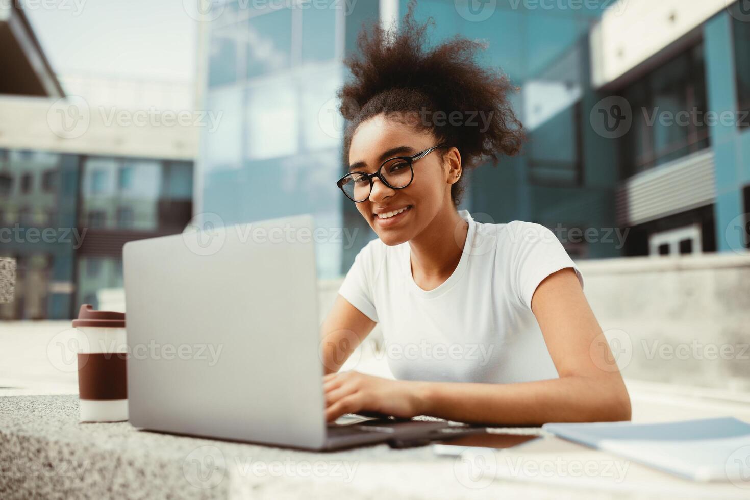 Successful Black Student Girl Using Laptop Computer Learning Online Watching Educational Webinar And Doing Homework Sitting Outdoor Near Urban University Building. Education And Studentship photo