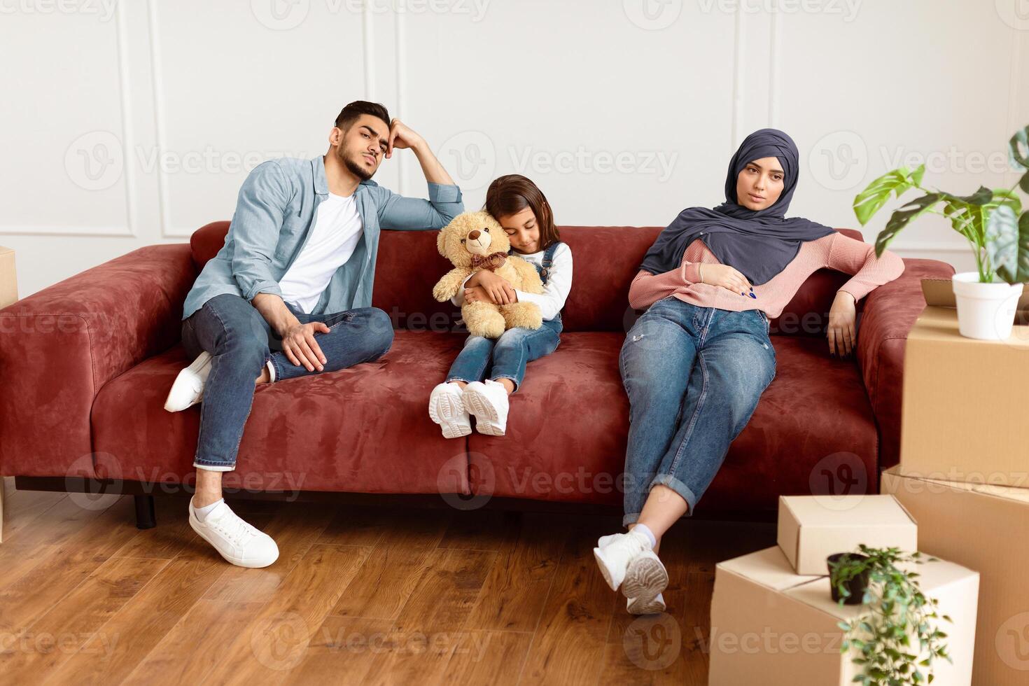 Sad upset Middle Eastern family feeling tired, leaving their house sitting on couch near carton boxes with personal belongings. Long hard relocation day, debt and eviction, physical exhaustion concept photo