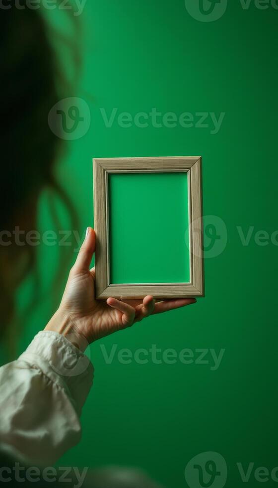 Hand holding picture frame with green screen on a plain green background photo
