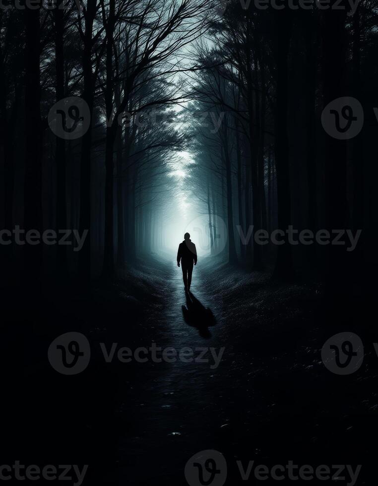 A solitary figure walks towards the light in a dark and mysterious forest path photo