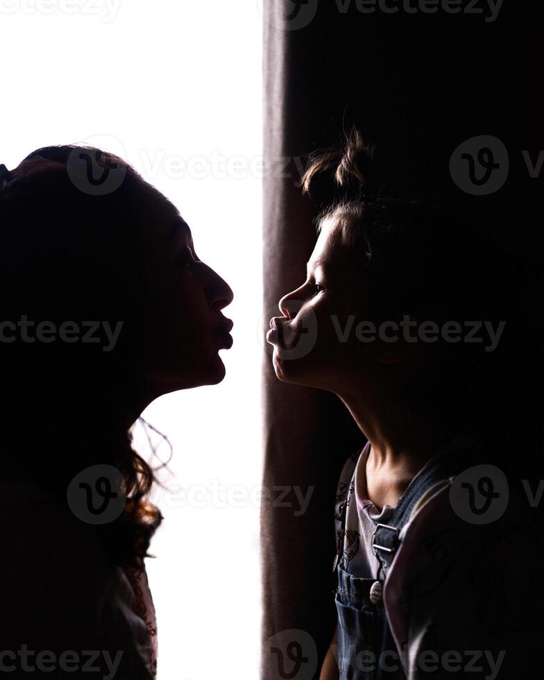 A silhouette portrait of a woman and a child kissing photo