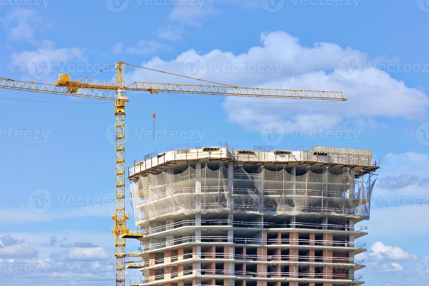 Construction with the help of a tower crane of the top of a multi-storey residential building using a monolithic-frame method against a blue cloudy sky. photo