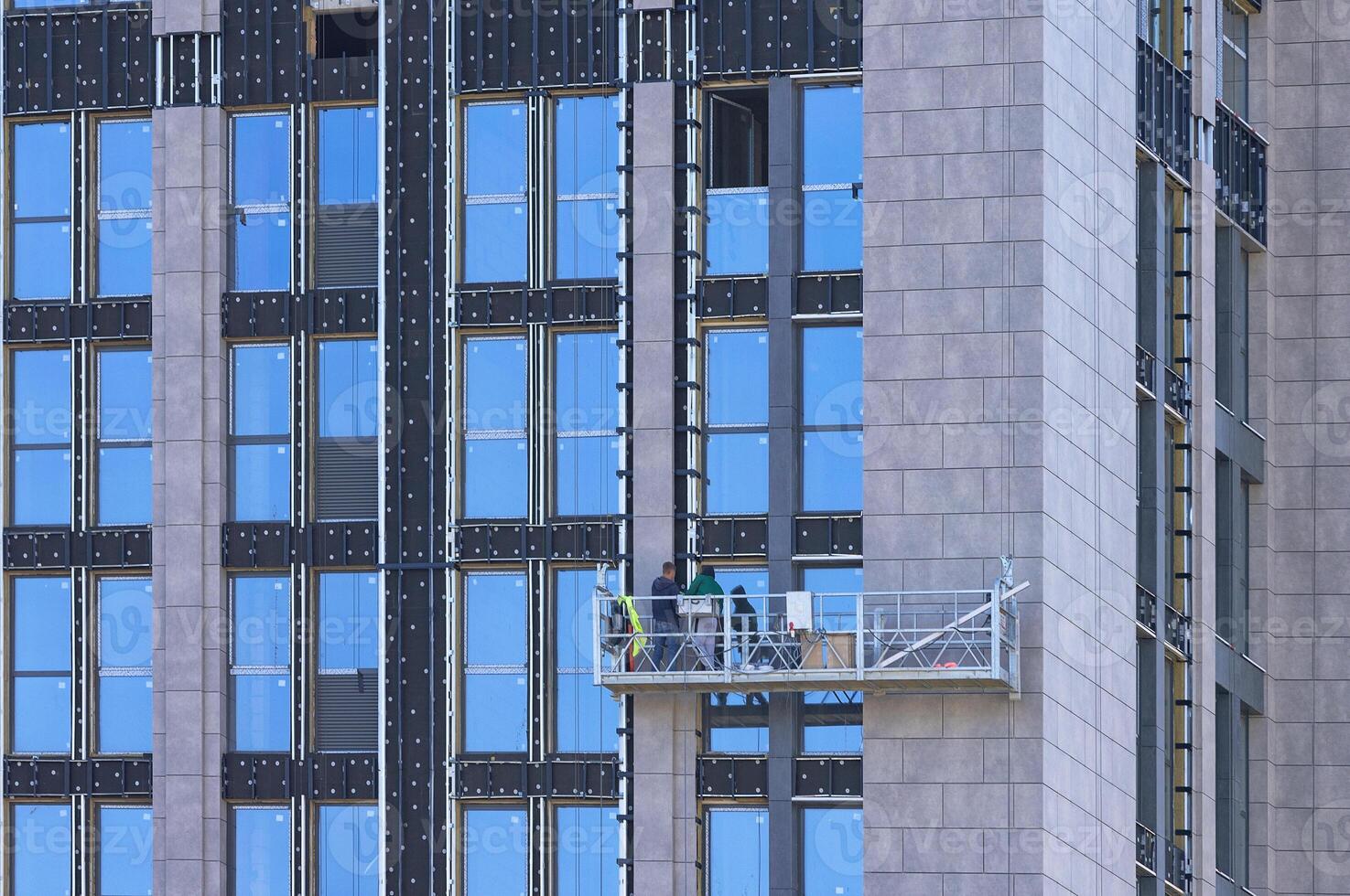 Builders on a suspended cradle mount decorative panels on the facade of a multi-storey skyscraper. photo