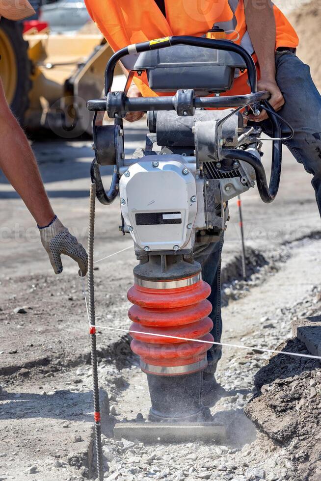 Construction workers using a compactor to prepare ground for building site in bright sunlight photo
